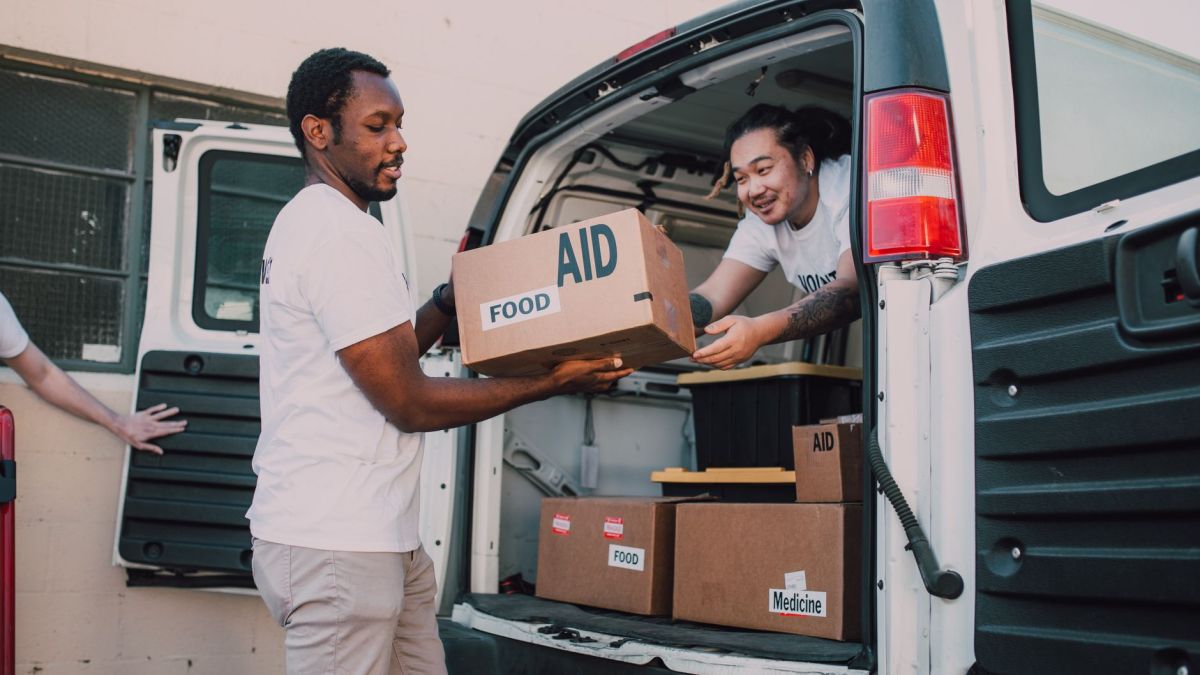 Two volunteers loading boxes labeled 'aid' into a van for community food donation drive.