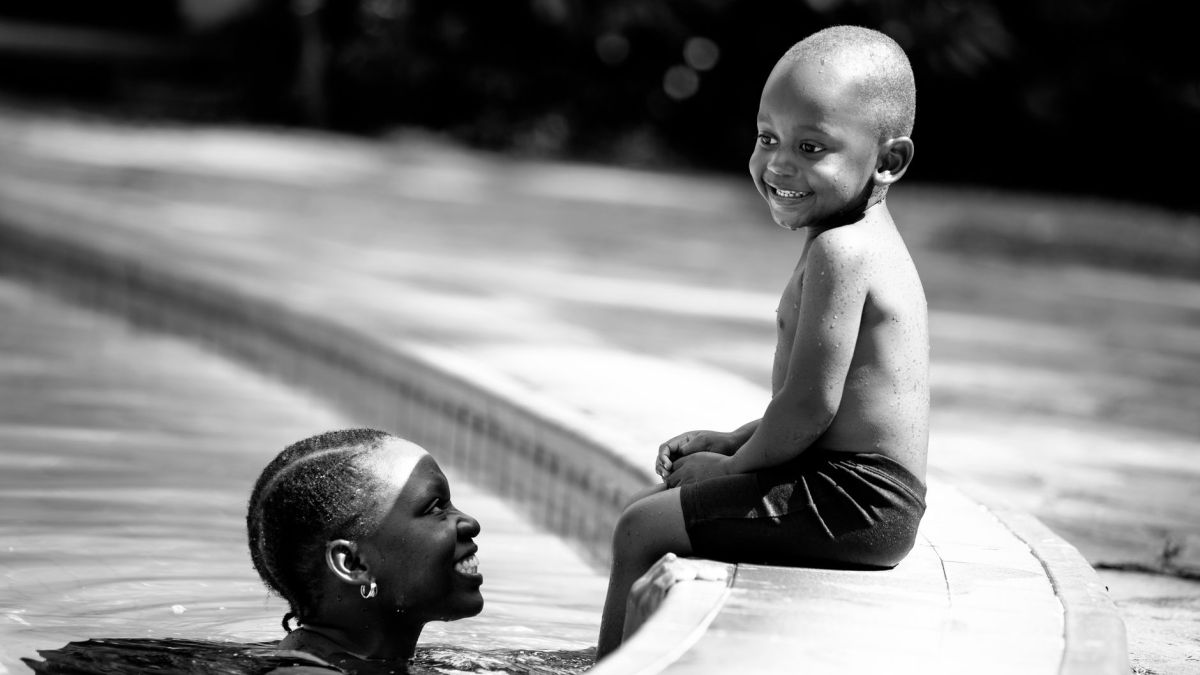 A joyful black and white photo of a mother and son by the swimming pool on a sunny day.