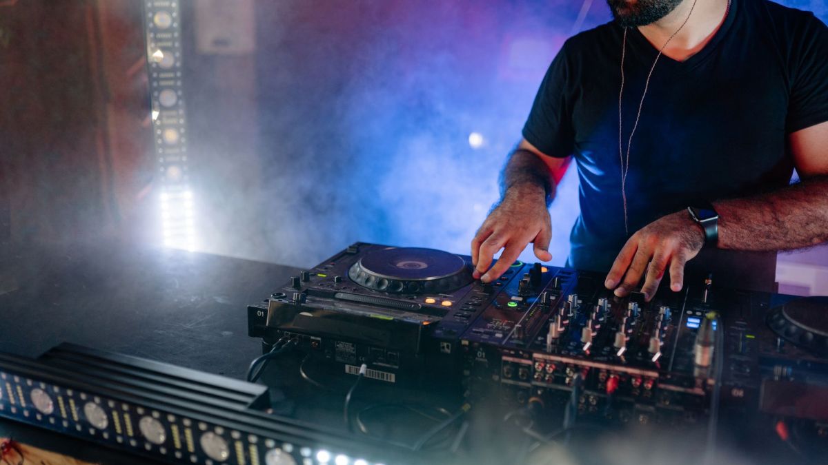 Energetic DJ performing live with mixing equipment in a colorful nightclub setting.