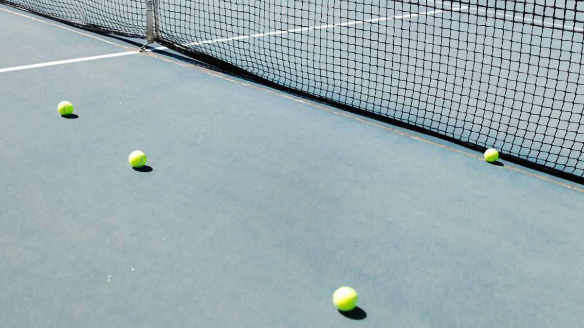 A tennis court featuring a net and several tennis balls lying on the ground, well-lit by sunlight.