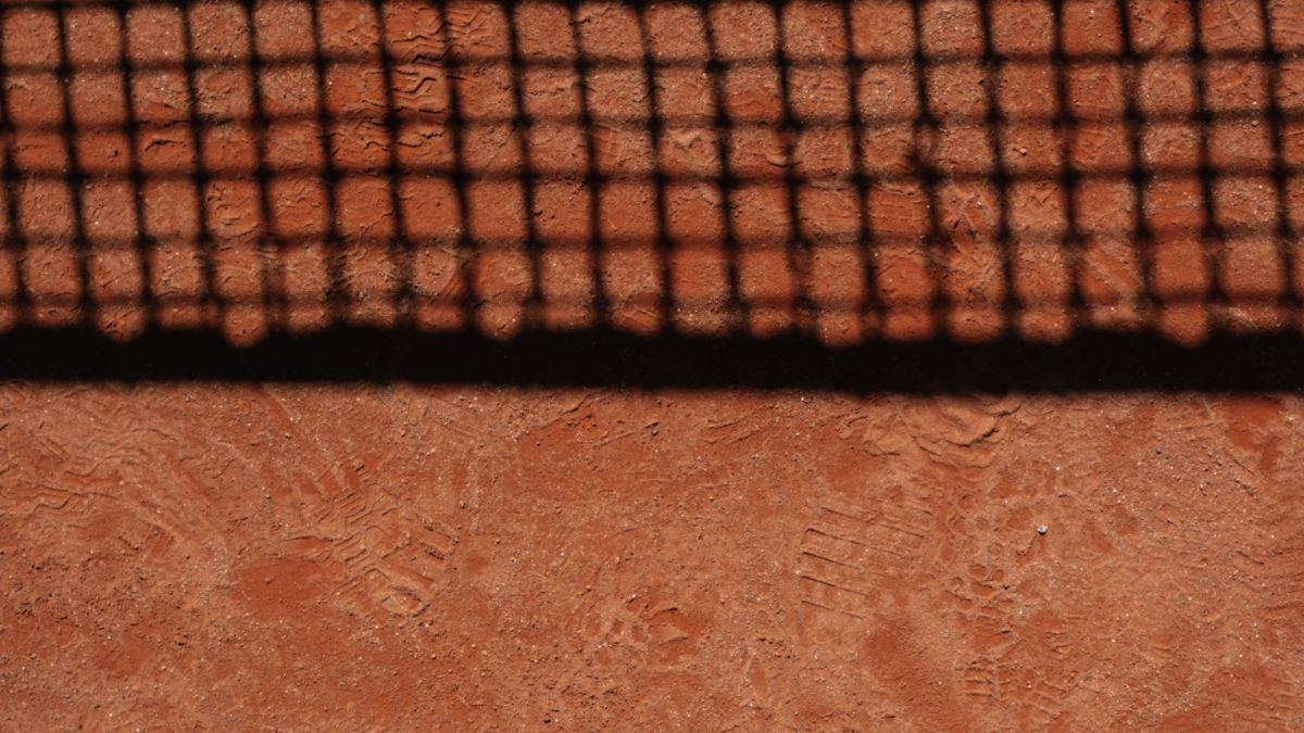 A close-up view of a tennis net shadow cast on a clay court showcasing detailed footprints.