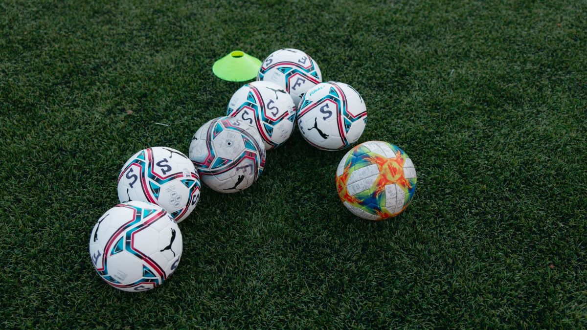 Group of soccer balls on a green grass field with a training cone, perfect for sports themes.