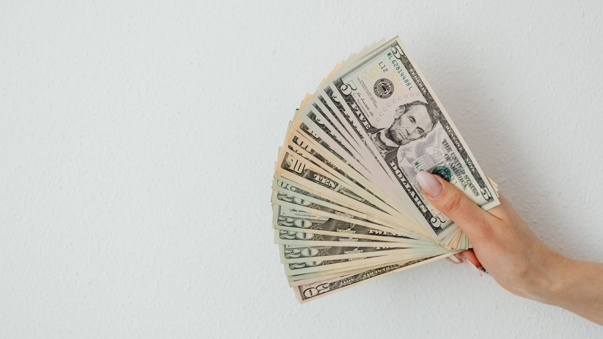 A hand holding an array of US dollar bills, fanned out against a plain white background.