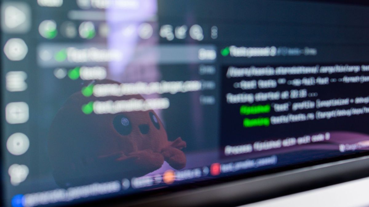 Close-up of a laptop screen displaying programming code with a cute plush toy reflecting.