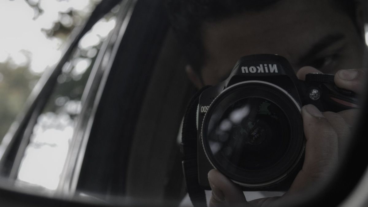 Reflective image of a photographer capturing with a camera in a car side mirror.