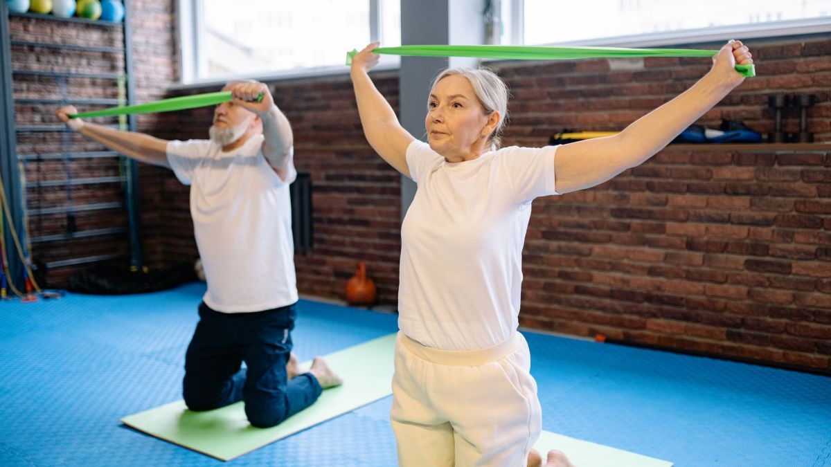 Elderly man and woman performing fitness workout with resistance bands, promoting healthy lifestyle indoors.
