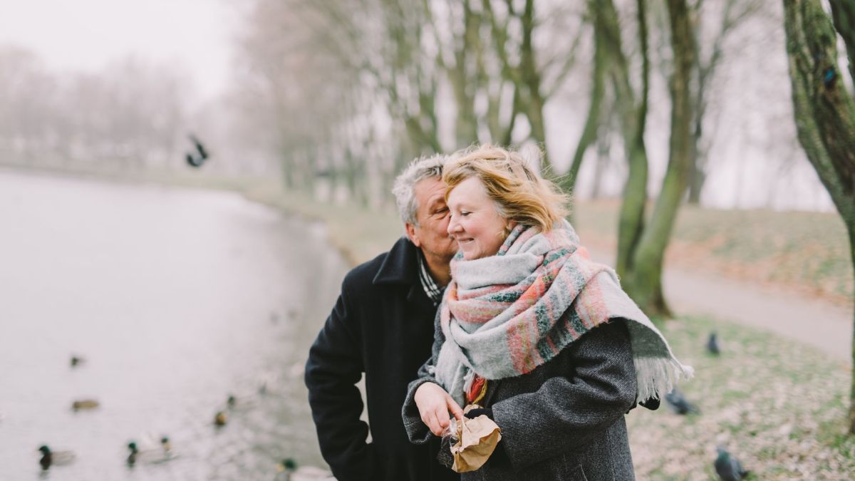 A senior couple walking by the lake, sharing a romantic moment in winter.