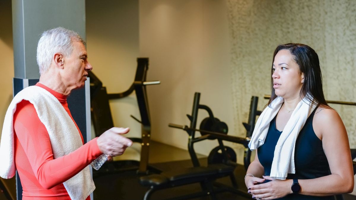 An elderly man and woman discuss fitness routines in a gym setting.