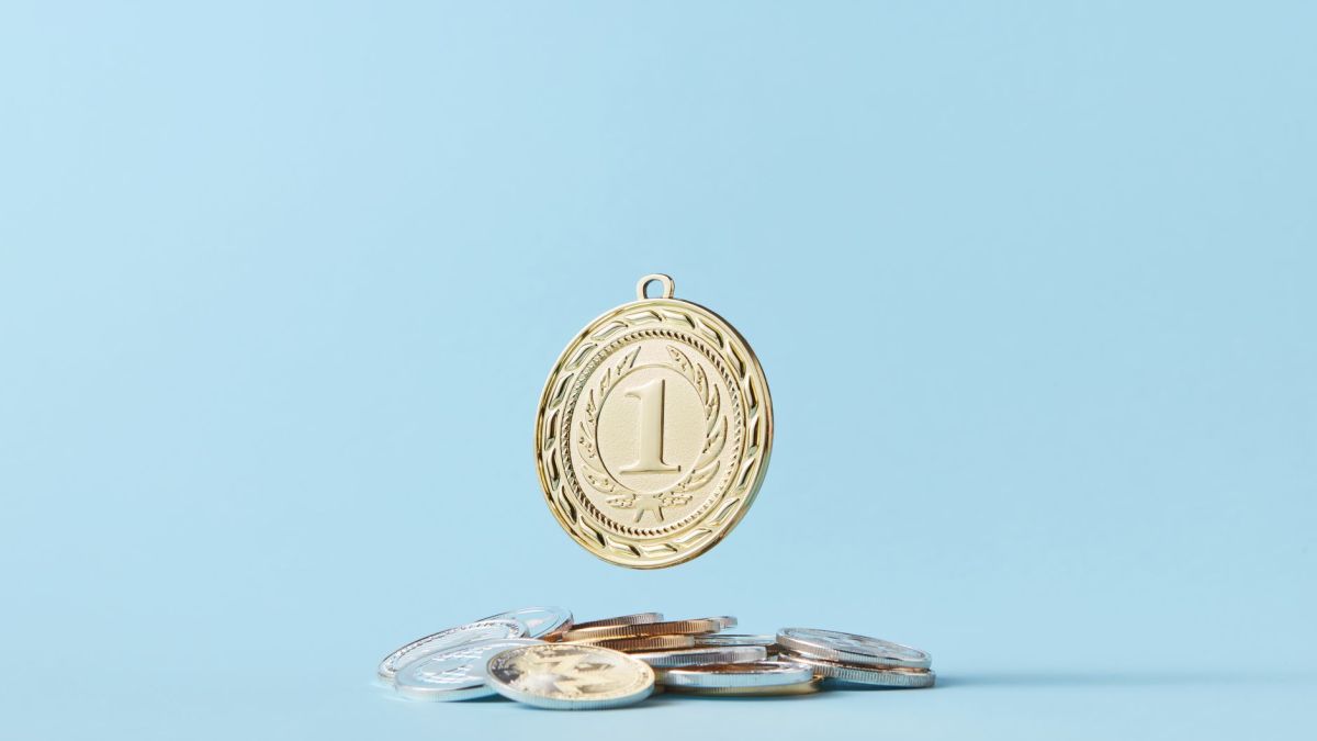 A gold medal and pile of coins on a light blue background representing achievement and savings.