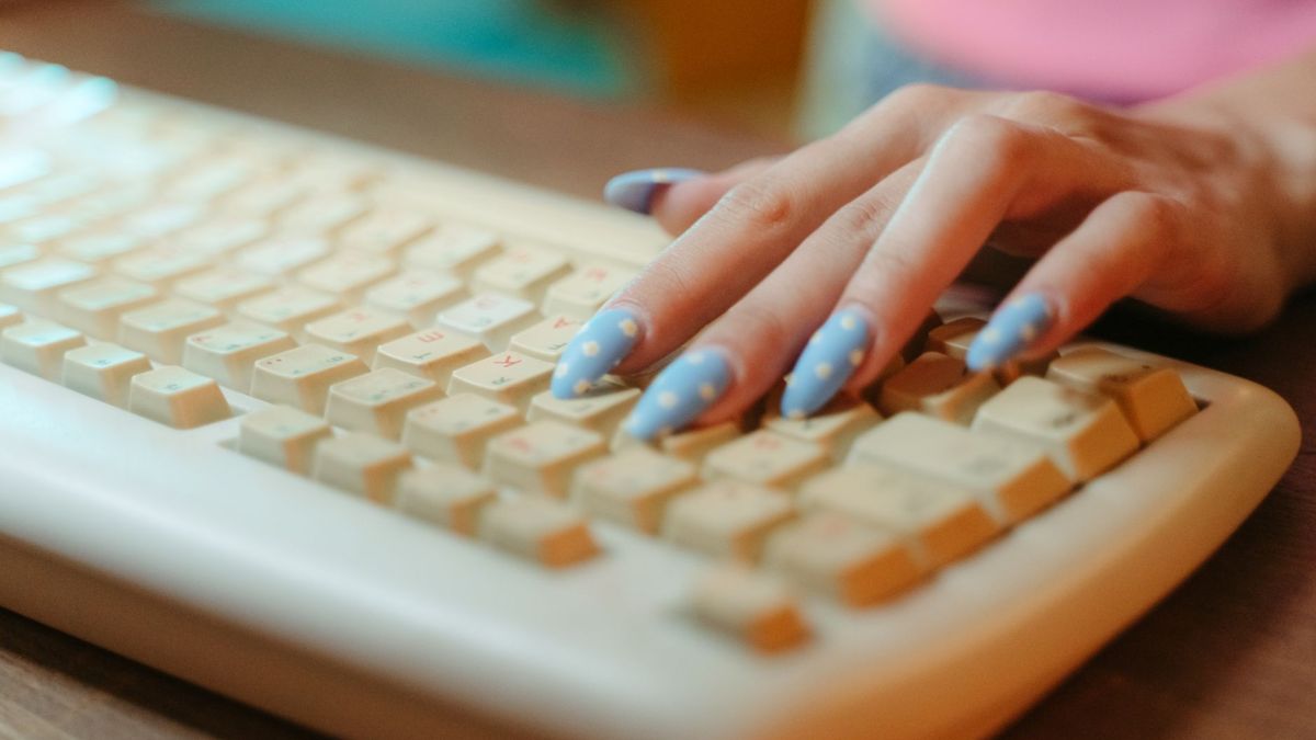 Closeup of a hand with polka dot nails typing on a vintage keyboard, emphasizing retro technology.