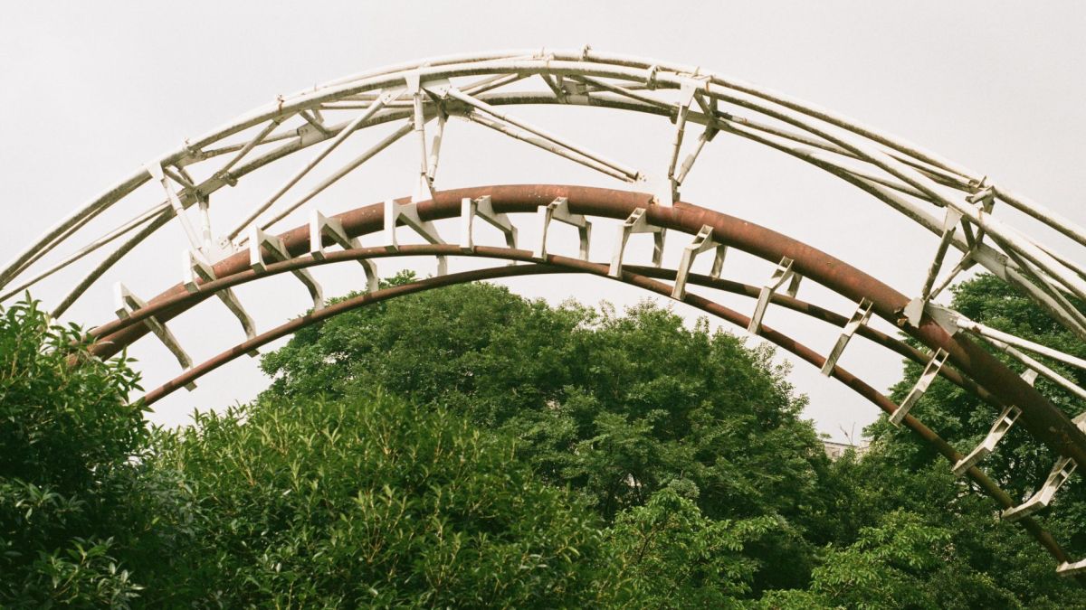 A close-up view of a steel roller coaster arch surrounded by lush summer foliage.