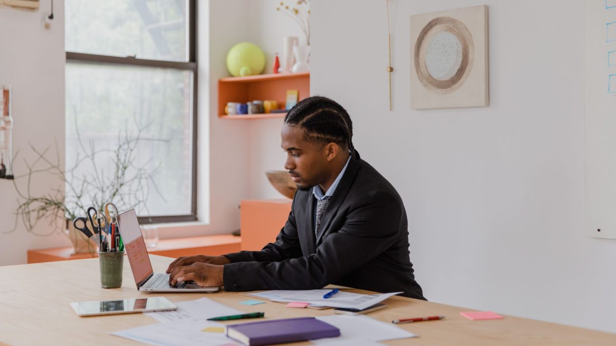 Professional businessman with braided hair working on a laptop at an office desk.