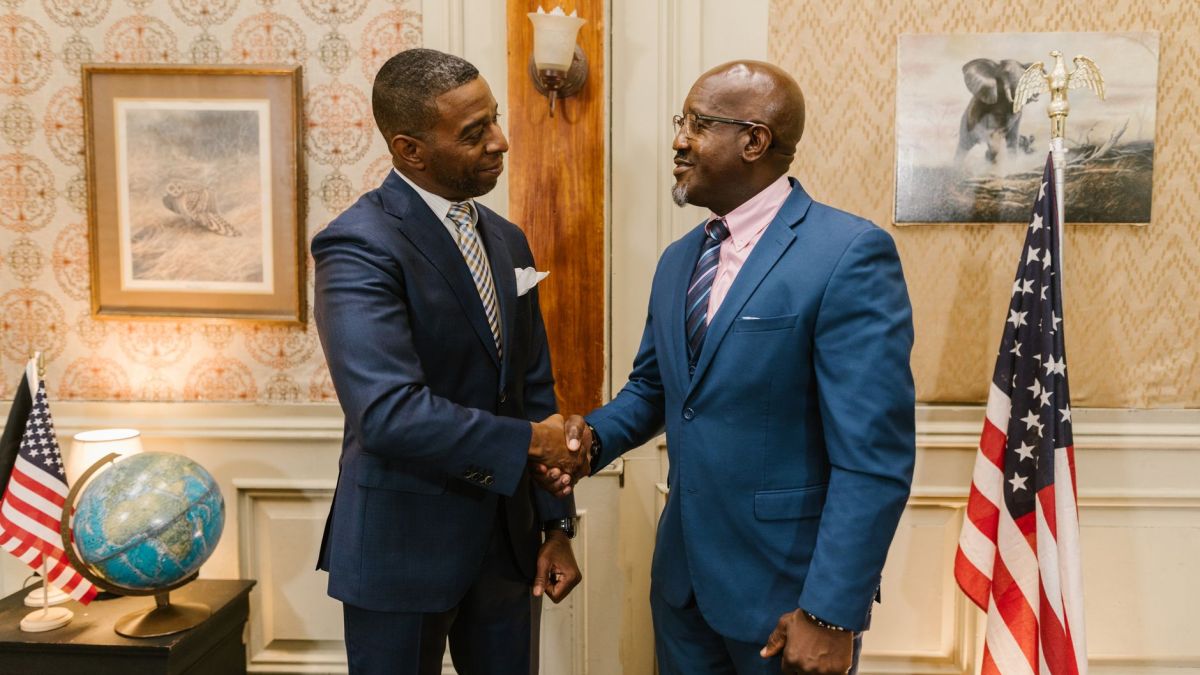 African American men in suits shaking hands in a formal law office setting with USA flags and globe.