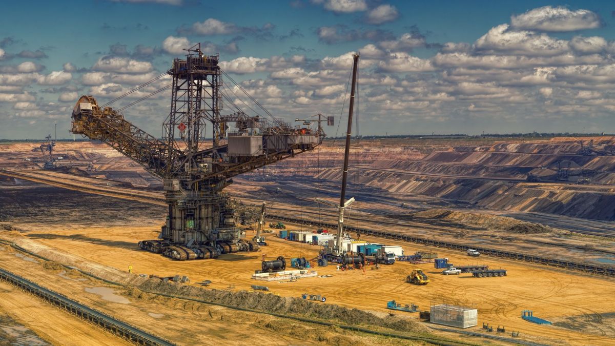 Aerial view of heavy machinery operating in a vast open-pit mine under a cloudy sky.