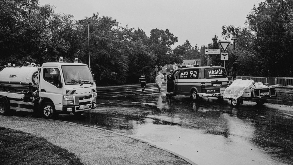 Black and white image of emergency vehicles on a rainy street with first responders.