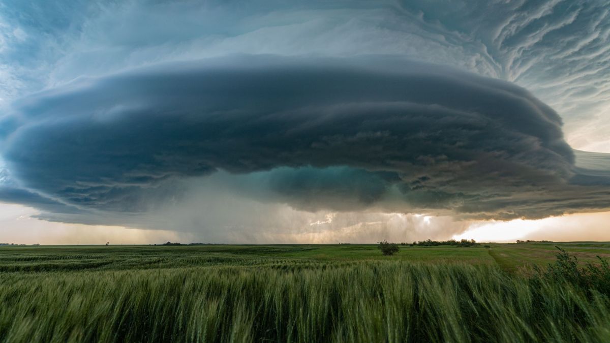 A powerful supercell storm looms over lush green fields in Saskatchewan, Canada.