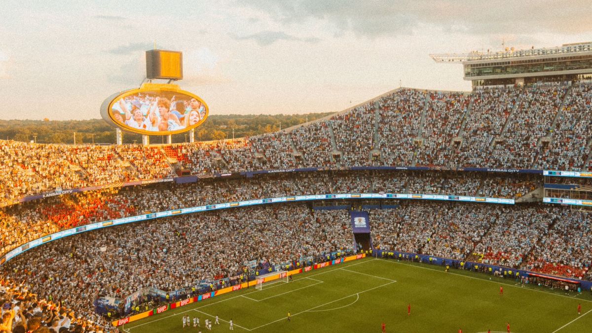 Aerial view of a packed soccer stadium during a lively match at sunset.