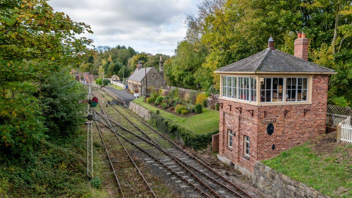 A tranquil rural railway station with signal box and tracks surrounded by autumn foliage.