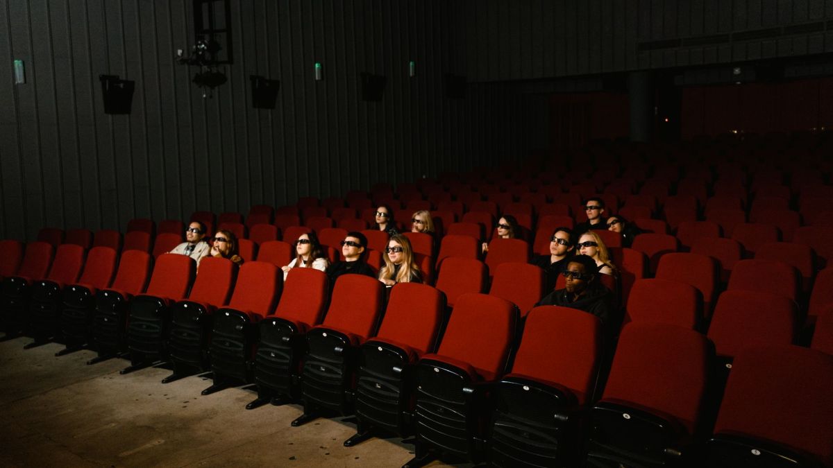 Small group of people wearing 3D glasses watching a movie in a theater with red seats.
