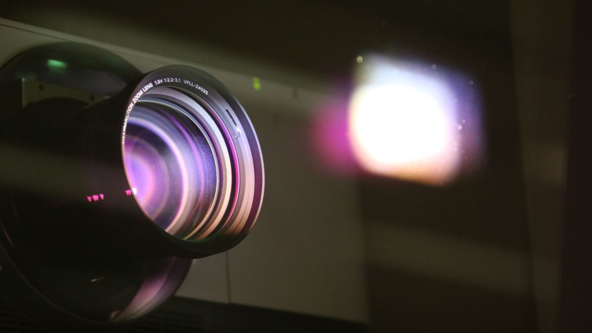 Close-up view of a projector lens with light reflections, highlighting optics and technology.