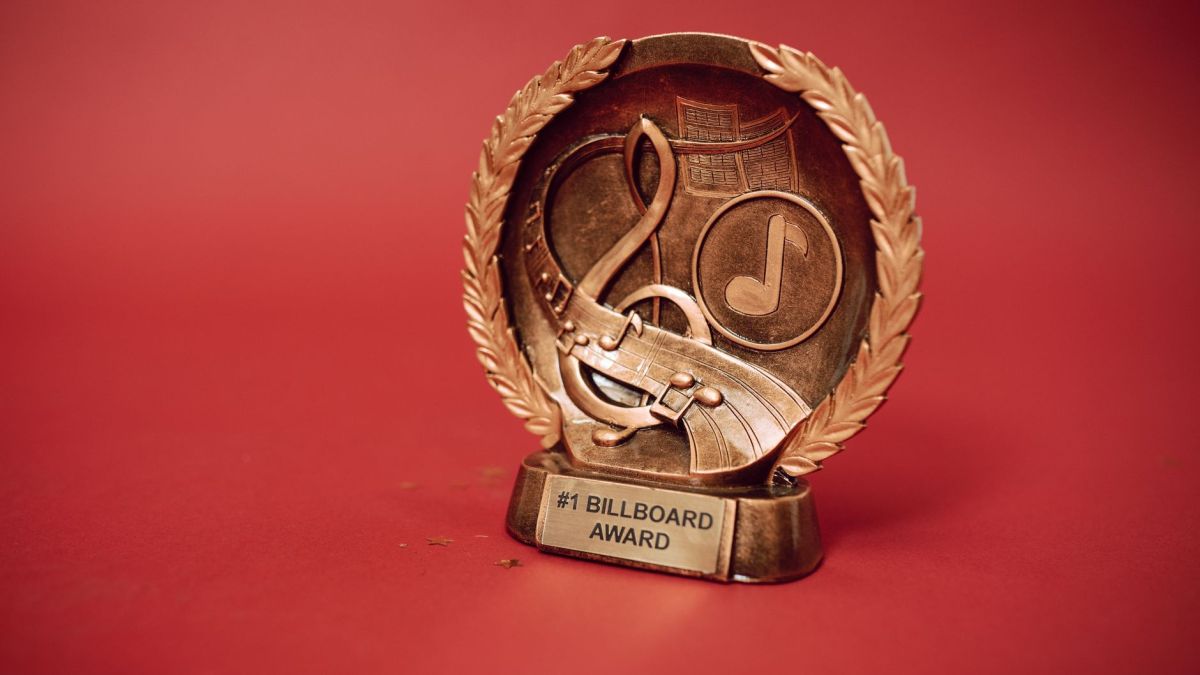 A close-up of a golden music award trophy against a vibrant red background.