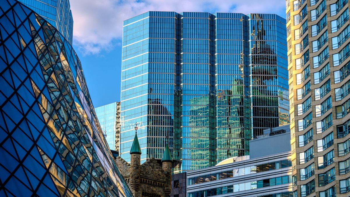 A vibrant cityscape featuring modern skyscrapers reflecting the blue sky and clouds.