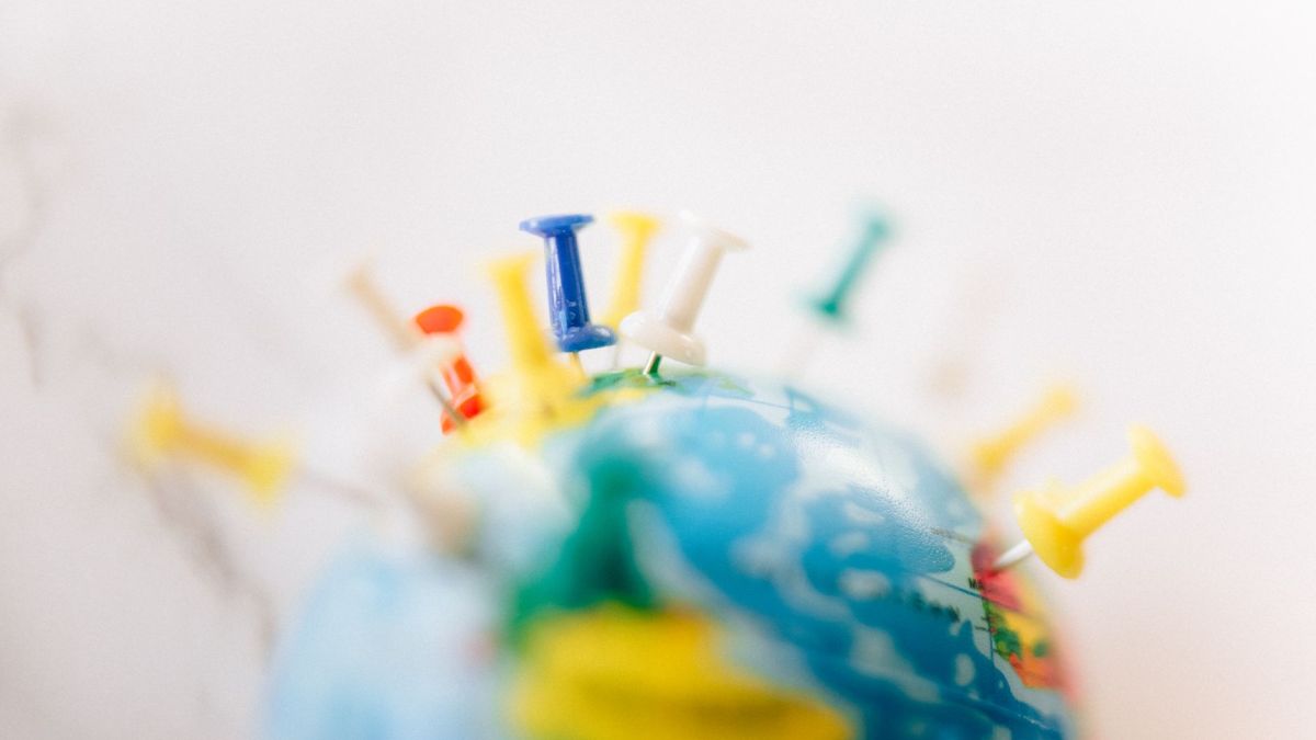 Vibrant close-up of a globe marked with multicolored push pins on a white background.