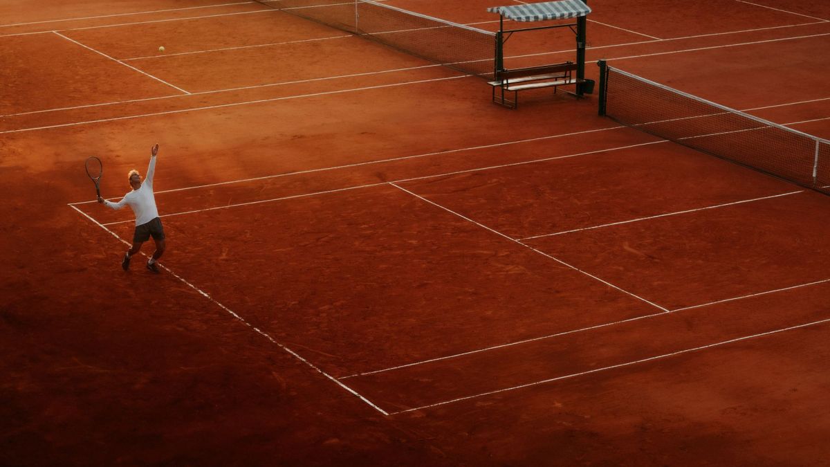A player serves on a clay tennis court, highlighting the beauty and intensity of the sport at sunset.