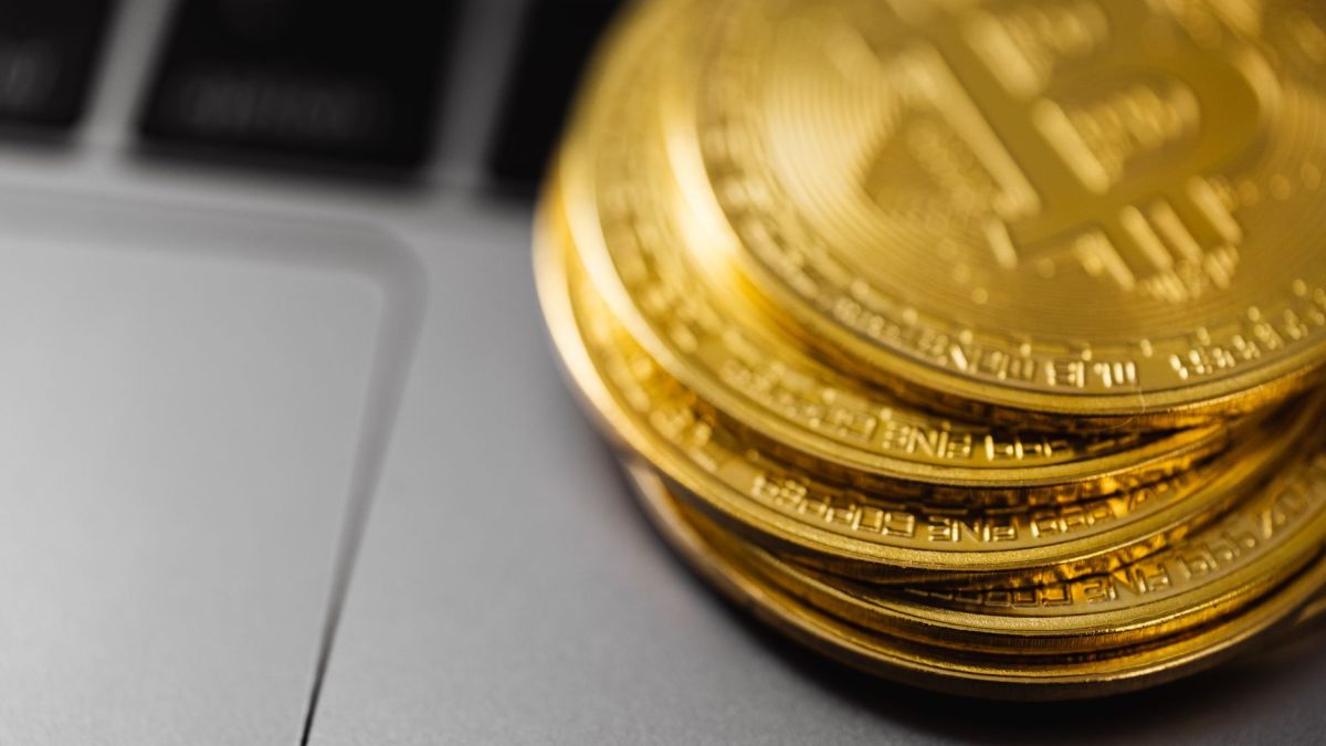 Stack of gold Bitcoin coins on a laptop keyboard, symbolizing digital currency technology and wealth.