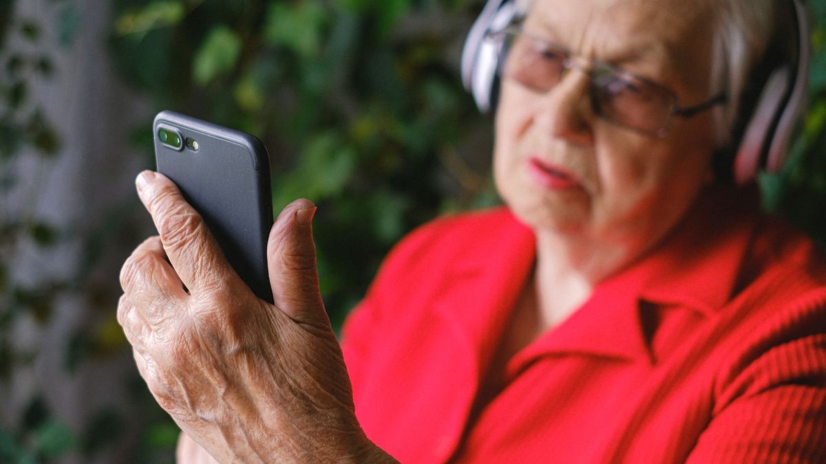 Senior woman in red using smartphone with headphones outdoors.