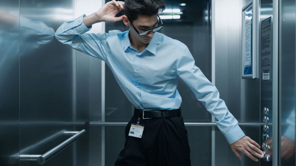 Stylish Asian man in office elevator adjusting his glasses, wearing professional attire.