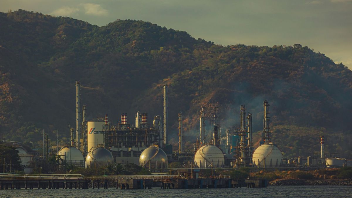 Industrial factory near mountains by a river, showcasing chimneys and infrastructure.