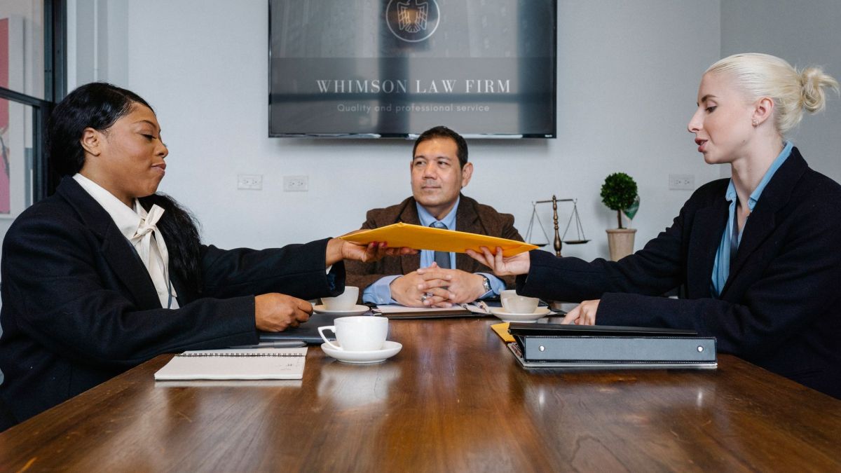 Group of cheerful diverse colleagues discussing court decision at table with notepad and cup