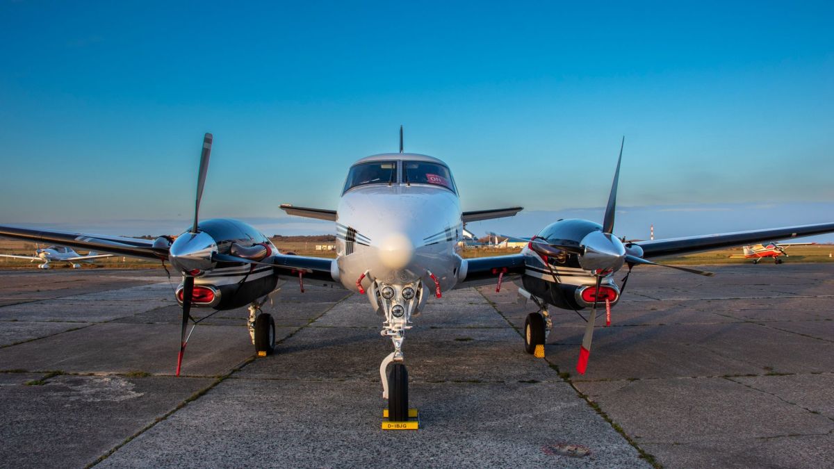 A front view of a twin-engine aircraft on tarmac under clear blue skies.