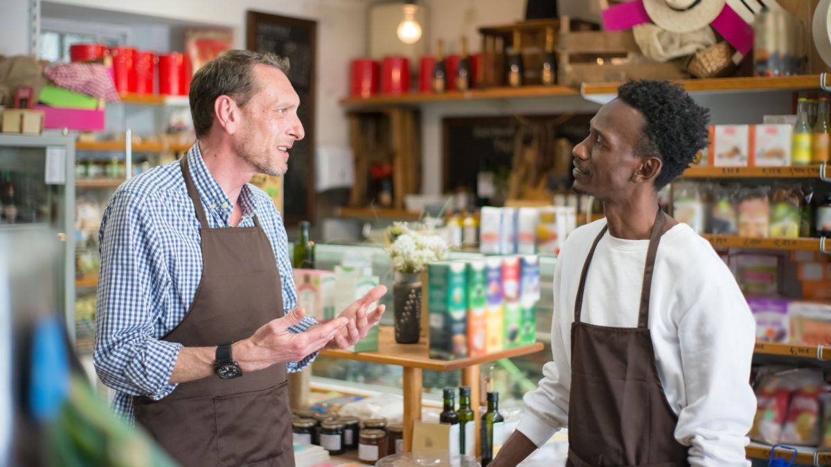 Two colleagues in aprons conversing in a grocery store setting.
