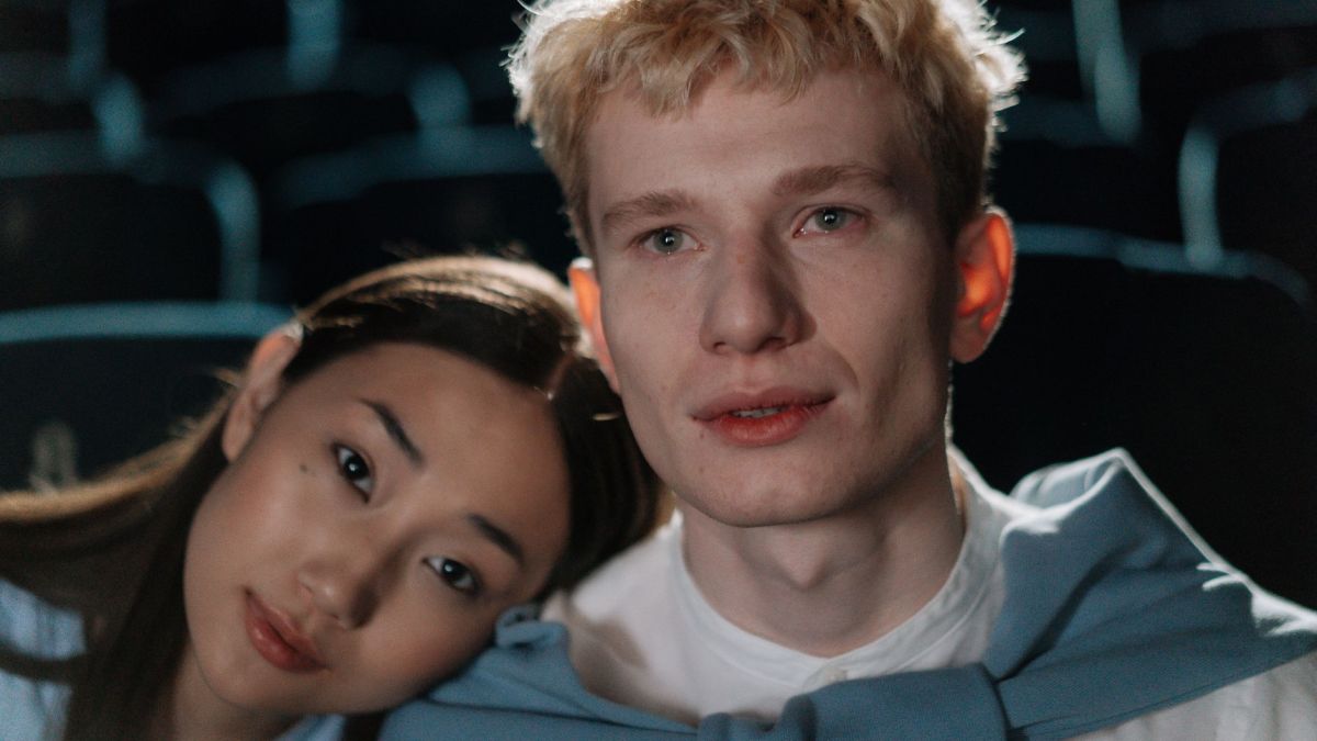 Close-up of a multicultural couple in a dimly lit theater, sharing a quiet moment.