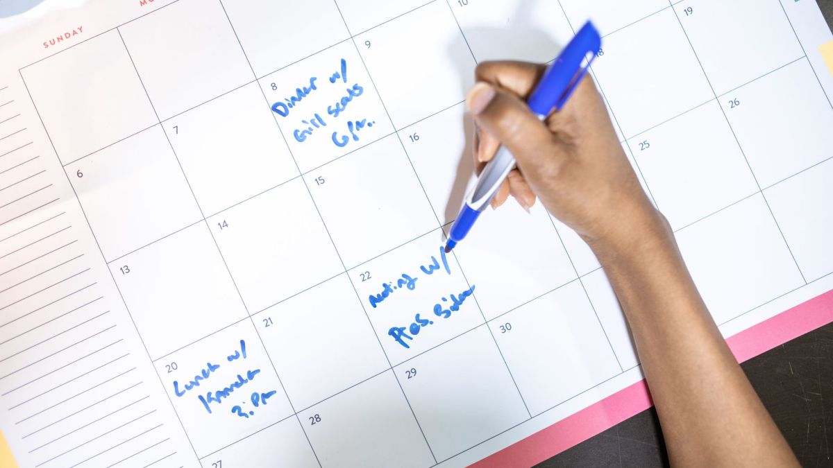 Person writing appointments on a calendar with a blue pen. High angle view.