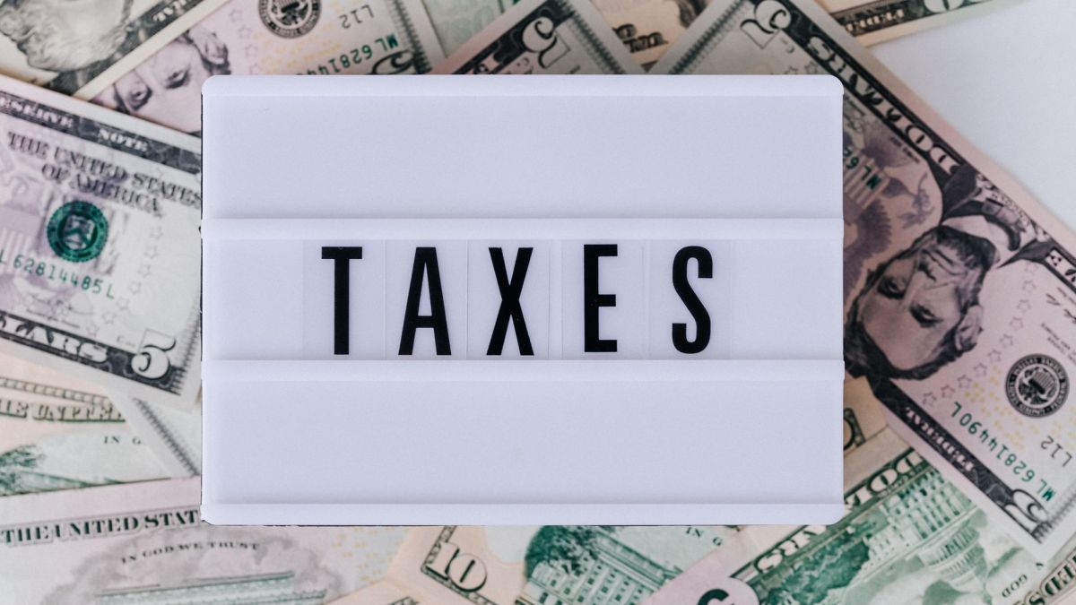Top view of white vintage light box with TAXES inscription placed on stack of USA dollar bills on white surface