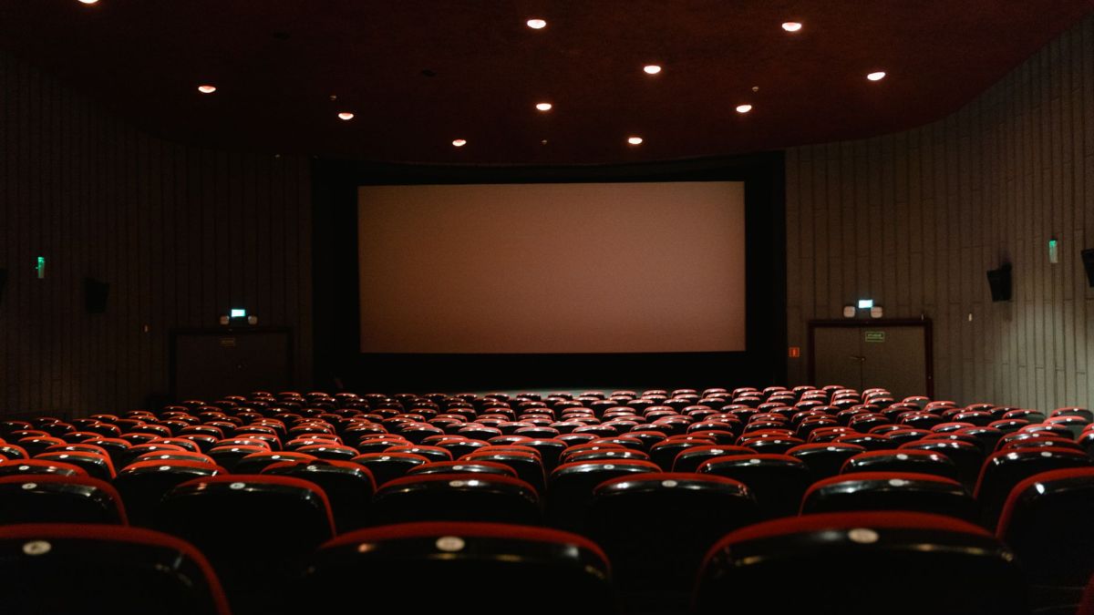 A dimly lit empty cinema theater with rows of red chairs facing a projector screen.