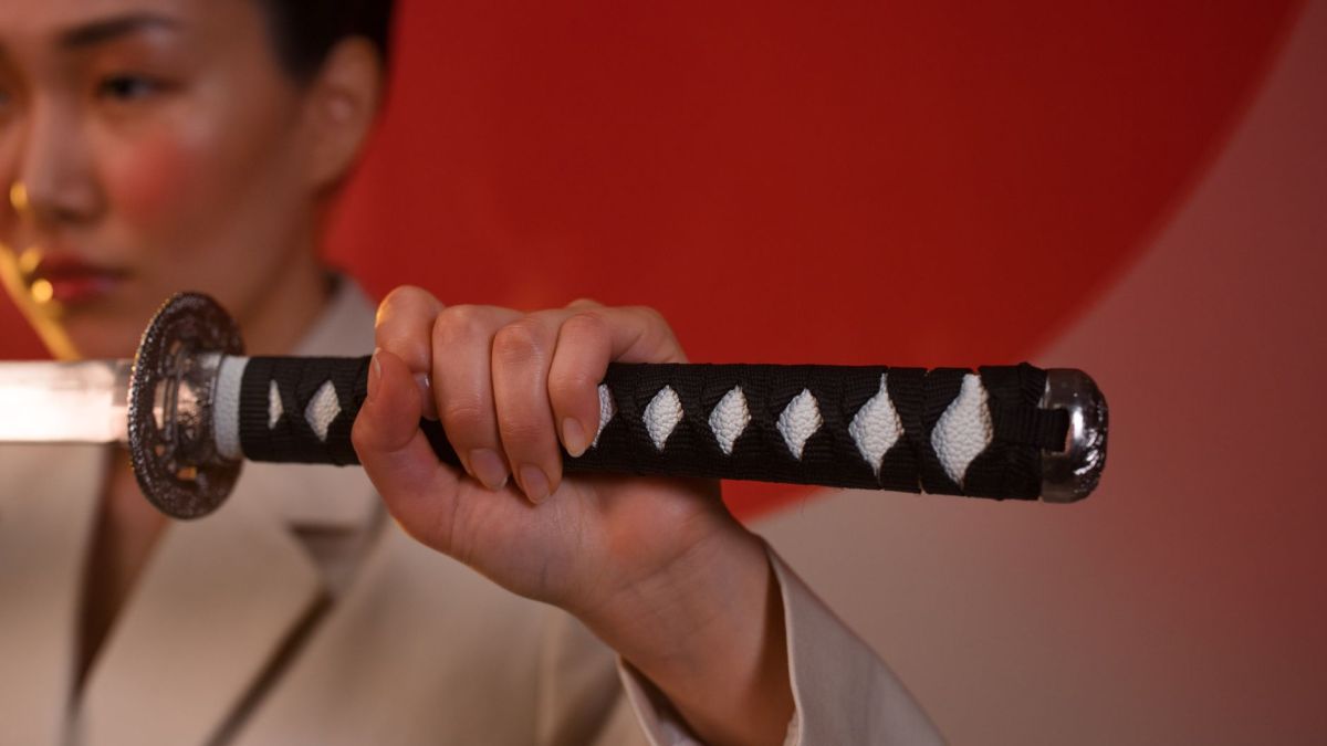 Close-up of a woman's hand gripping a sword against a vibrant red backdrop.