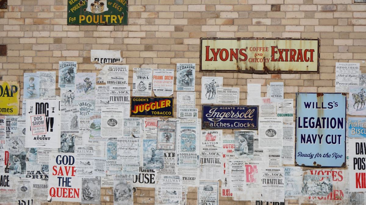 A collection of vintage posters on a brick wall, showcasing historic advertisements and text.