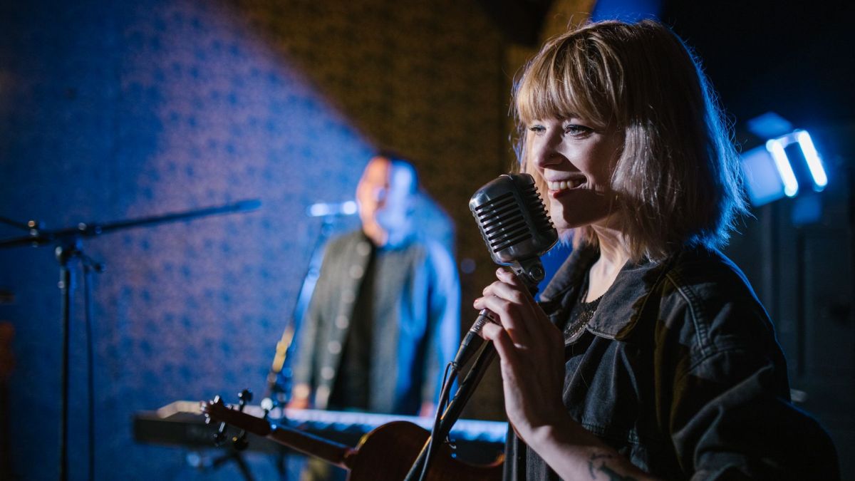 Smiling caucasian woman singing with vintage microphone during live music performance.