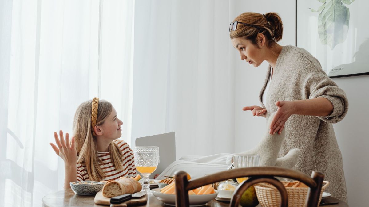 A mother and teenage daughter having a discussion while having breakfast at home.