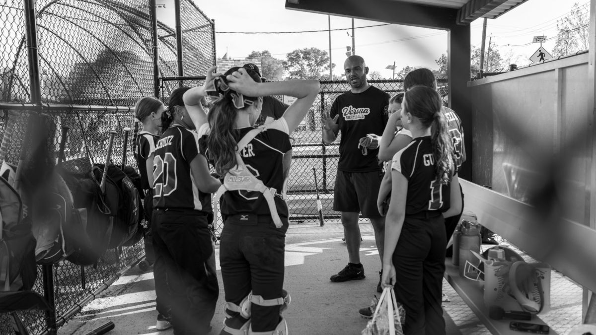 A youth softball coach gives a team talk to players in a dugout at Verona, NJ. Black and white photo.