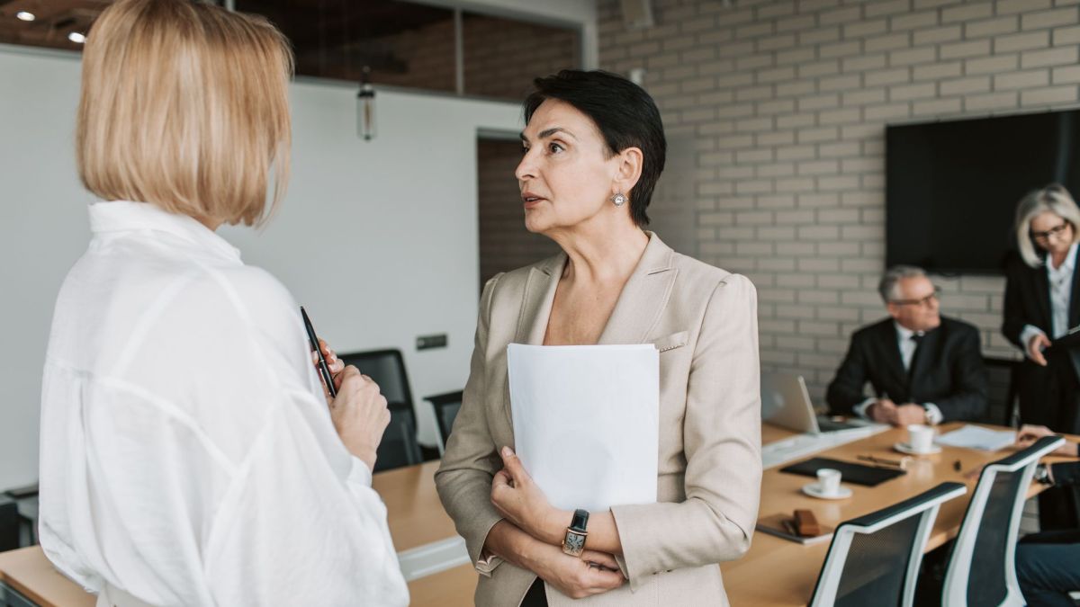 Two businesswomen engage in a conversation during a professional meeting in a modern office.