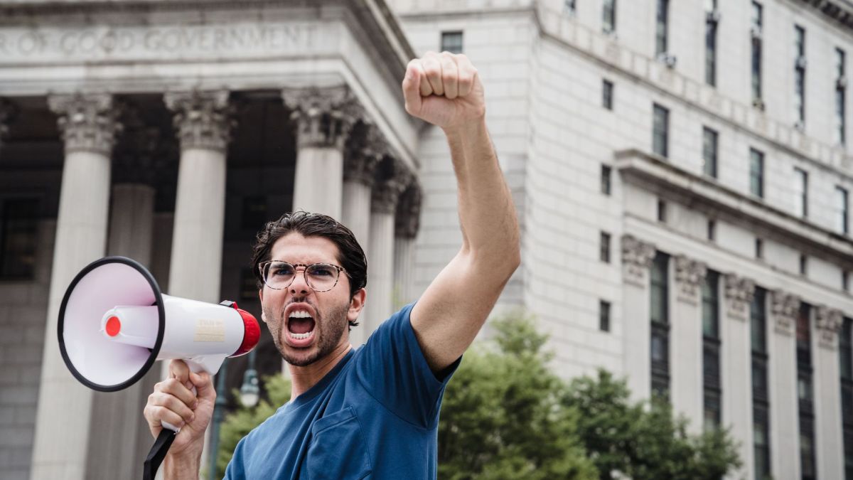 Man passionately protesting with a megaphone in front of a historic building, symbolizing activism.