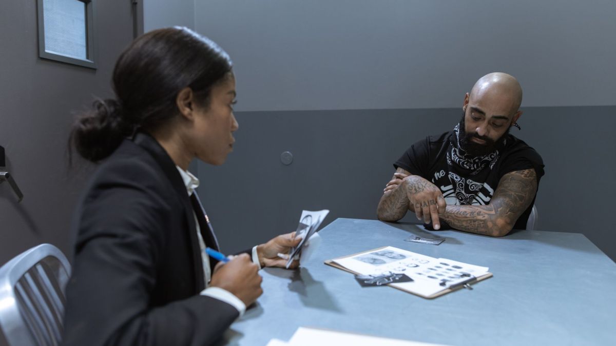 Police officer interrogating a suspect in an investigation room with documents and evidence on the table.