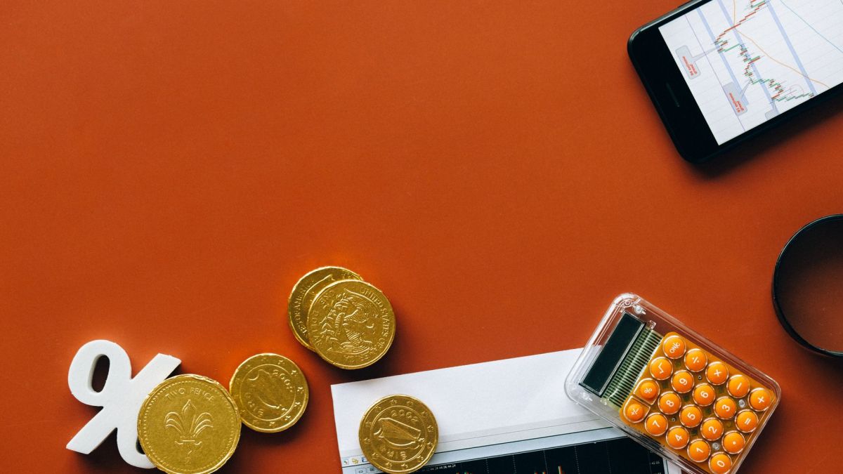 Flat lay showing coins, calculator, and charts on a red background for financial analysis and business concepts.