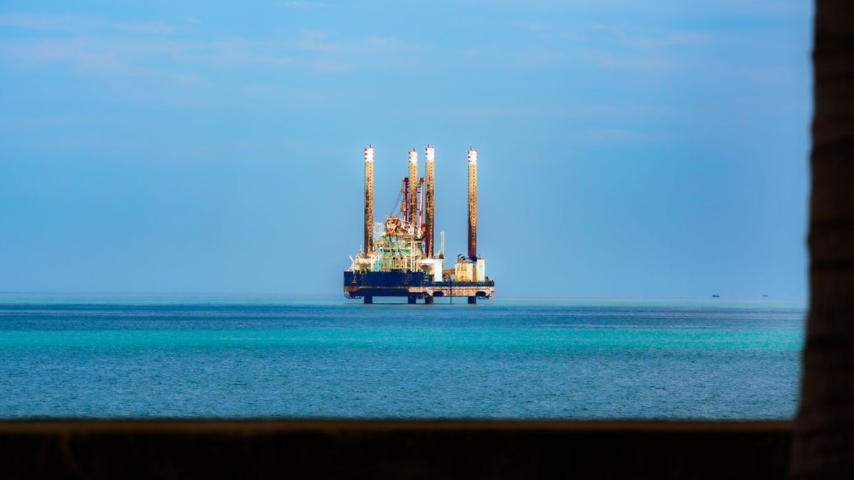Distant view of an offshore oil rig in a calm, blue ocean under a clear sky.