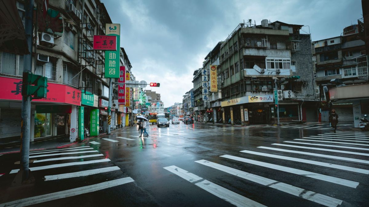 Overcast sky with pedestrians on a wet city street crossing in a bustling urban area.